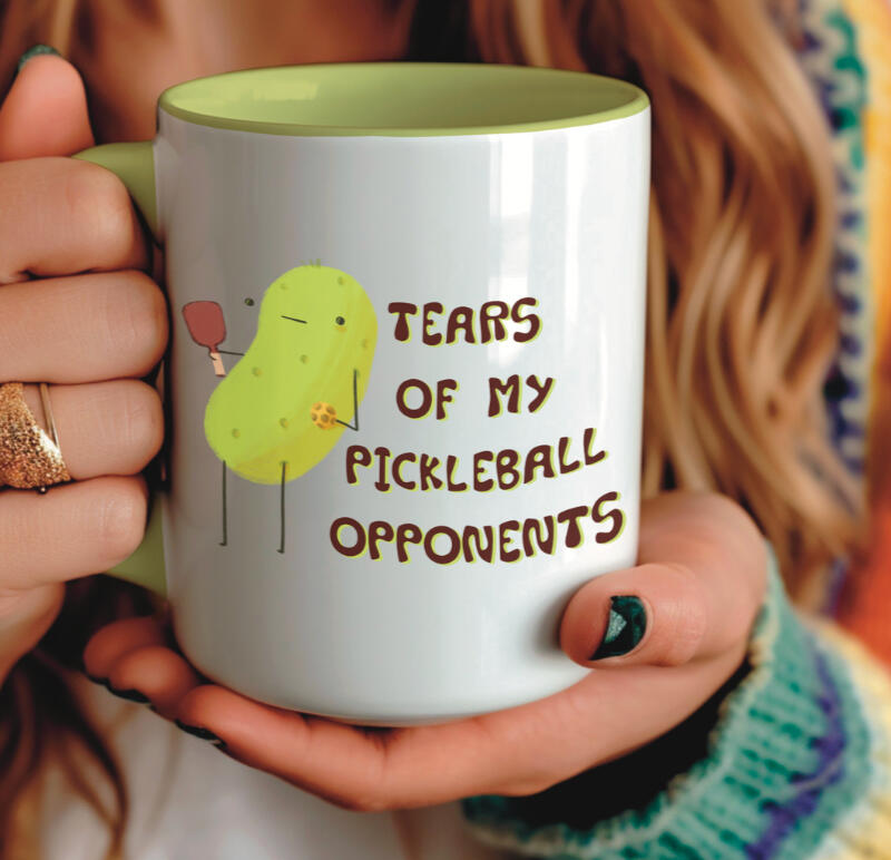 Spot illustration for licensing on a coffee mug that is a pickle with a pickleball paddle next to text that says "tears of my pickleball opponents"